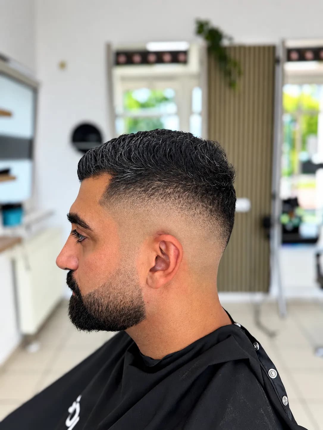 Herrenschnitt mit sauberem Fade und gepflegtem Vollbart, Seitenansicht im Salon